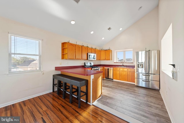 kitchen featuring kitchen peninsula, dark hardwood / wood-style floors, stainless steel appliances, a kitchen breakfast bar, and sink