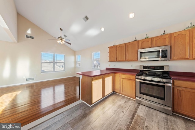 kitchen featuring appliances with stainless steel finishes, kitchen peninsula, ceiling fan, high vaulted ceiling, and dark hardwood / wood-style floors