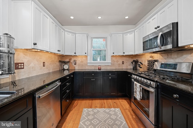 kitchen featuring light hardwood / wood-style flooring, stainless steel appliances, tasteful backsplash, white cabinetry, and dark stone countertops