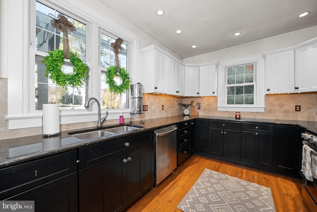 kitchen featuring stainless steel appliances, light hardwood / wood-style floors, dark stone countertops, and sink