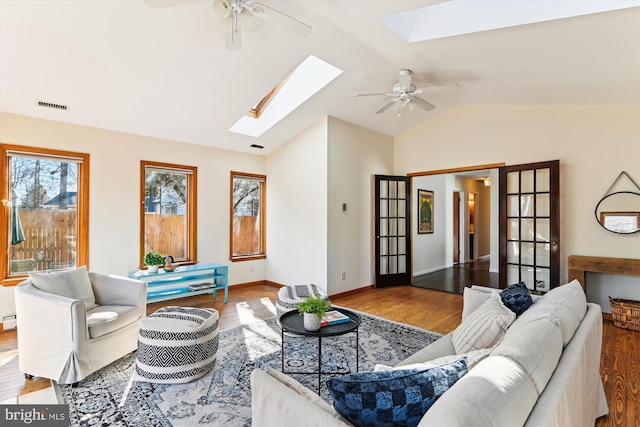 living room with hardwood / wood-style floors, vaulted ceiling with skylight, and ceiling fan