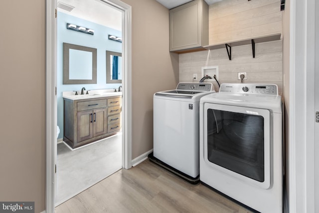 laundry room featuring sink, cabinets, light hardwood / wood-style flooring, wooden walls, and independent washer and dryer