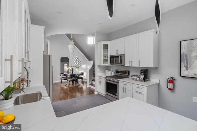 kitchen with stainless steel appliances, sink, white cabinets, and light stone countertops