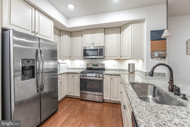 kitchen with appliances with stainless steel finishes, hardwood / wood-style floors, sink, white cabinets, and light stone countertops