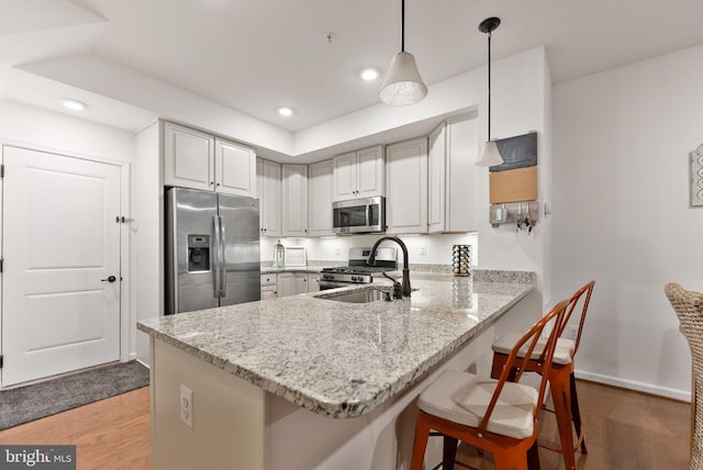 kitchen featuring appliances with stainless steel finishes, decorative light fixtures, light stone counters, kitchen peninsula, and light wood-type flooring