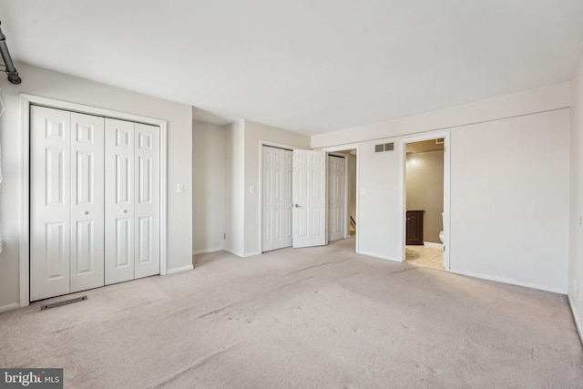 unfurnished bedroom featuring connected bathroom, light carpet, and two closets