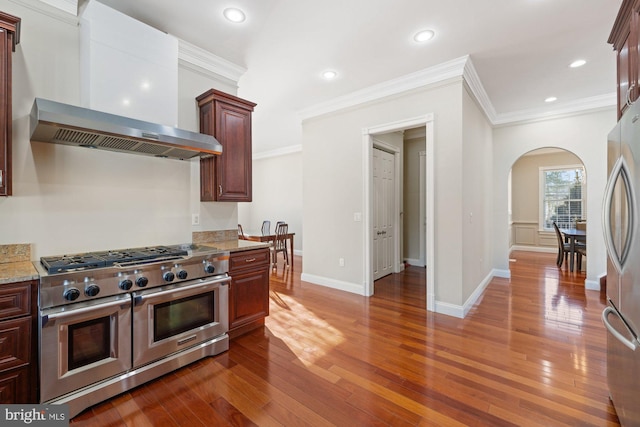 kitchen featuring appliances with stainless steel finishes, wall chimney exhaust hood, light stone countertops, and wood-type flooring