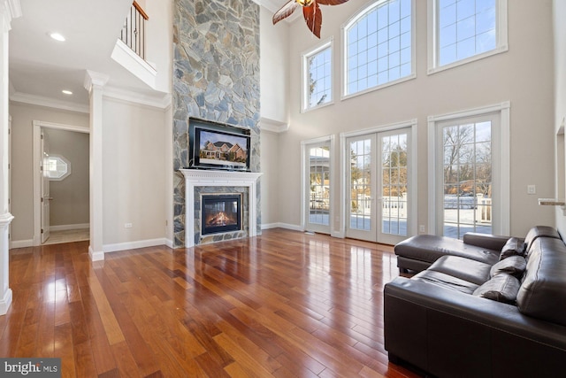 living room with hardwood / wood-style floors, a stone fireplace, ornamental molding, and ceiling fan