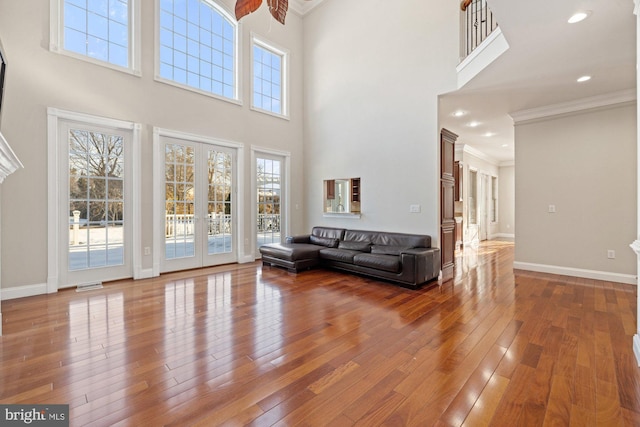 unfurnished living room featuring hardwood / wood-style floors, a towering ceiling, ornamental molding, and french doors