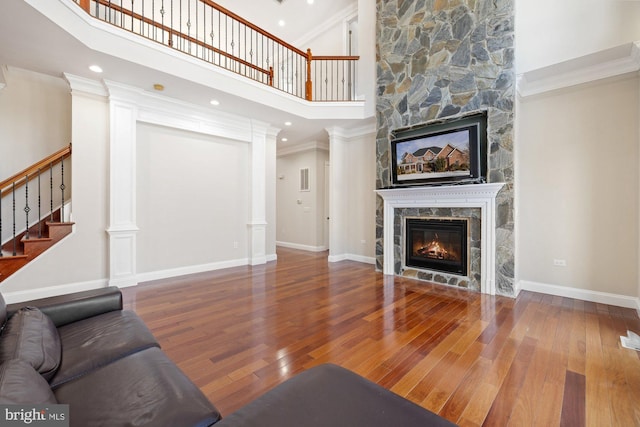 living room featuring hardwood / wood-style floors, a fireplace, decorative columns, a high ceiling, and ornamental molding