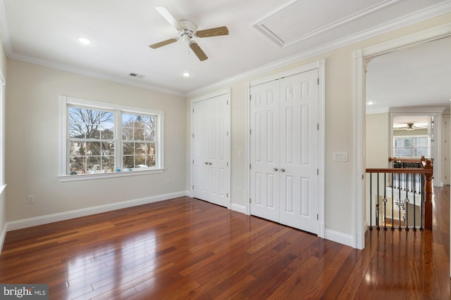 unfurnished bedroom featuring crown molding, ceiling fan, dark hardwood / wood-style flooring, and two closets