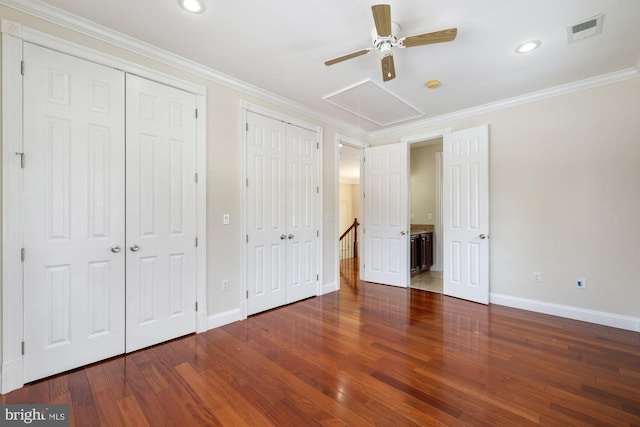 unfurnished bedroom featuring crown molding, dark wood-type flooring, two closets, and ceiling fan