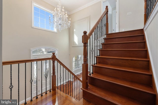 staircase featuring crown molding, a towering ceiling, wood-type flooring, and an inviting chandelier