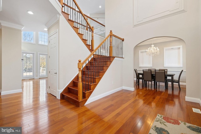 staircase with crown molding, hardwood / wood-style floors, a towering ceiling, and a notable chandelier