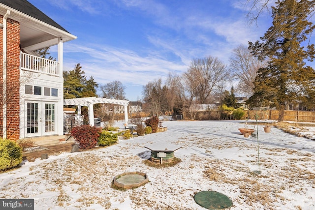 snowy yard featuring french doors, a balcony, and a pergola