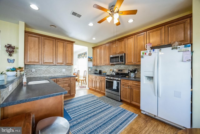 kitchen featuring a sink, dark countertops, appliances with stainless steel finishes, brown cabinetry, and light wood finished floors