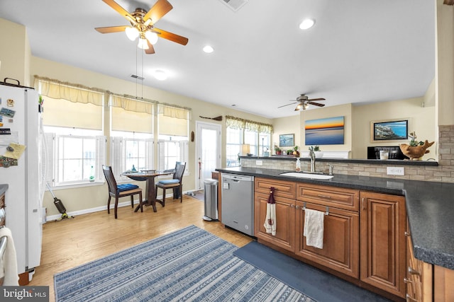 kitchen featuring a wealth of natural light, brown cabinets, a sink, freestanding refrigerator, and dishwasher