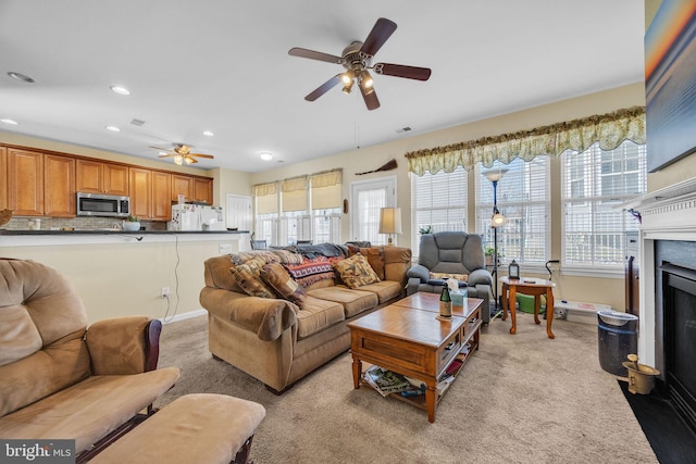 living area with a fireplace with flush hearth, light colored carpet, baseboards, and a ceiling fan