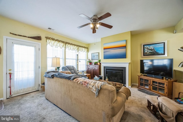 carpeted living area with visible vents, a glass covered fireplace, and a ceiling fan