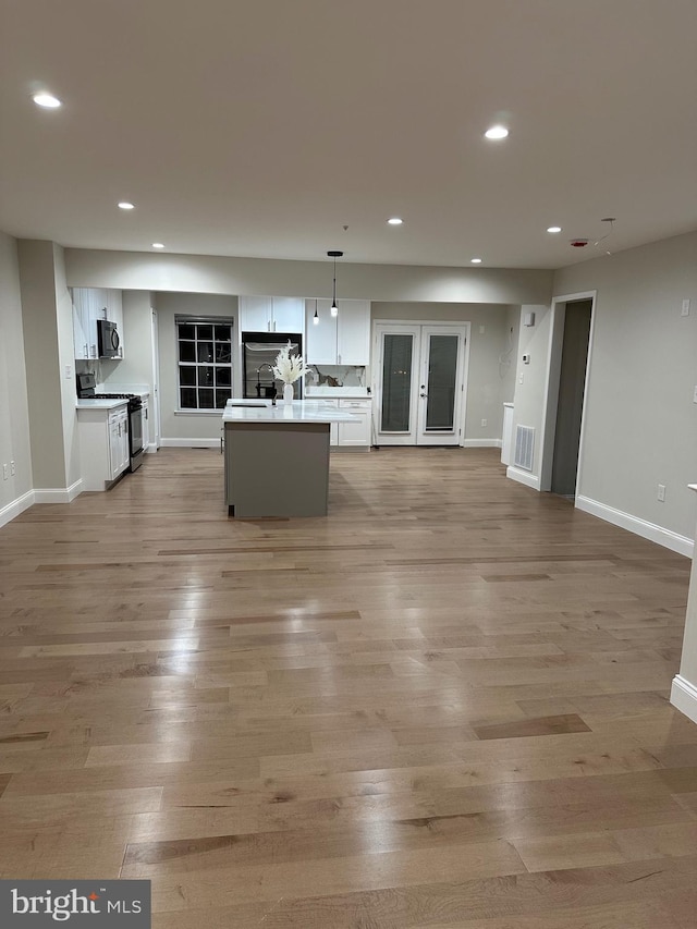 kitchen featuring a center island with sink, white cabinetry, stainless steel range with gas stovetop, and pendant lighting