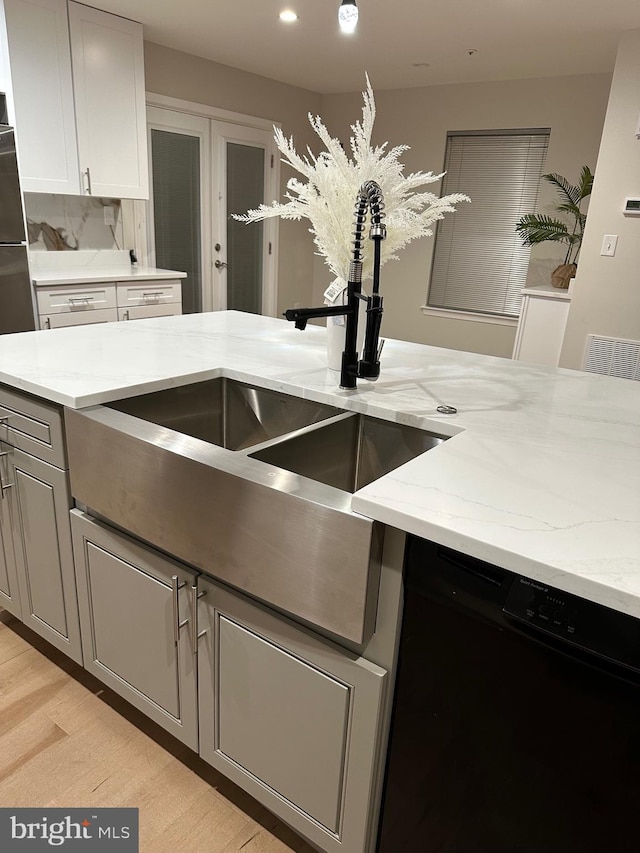 kitchen with sink, dishwasher, light stone counters, french doors, and light wood-type flooring