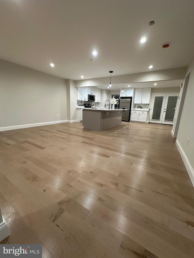 kitchen with pendant lighting, white cabinetry, an island with sink, sink, and light wood-type flooring