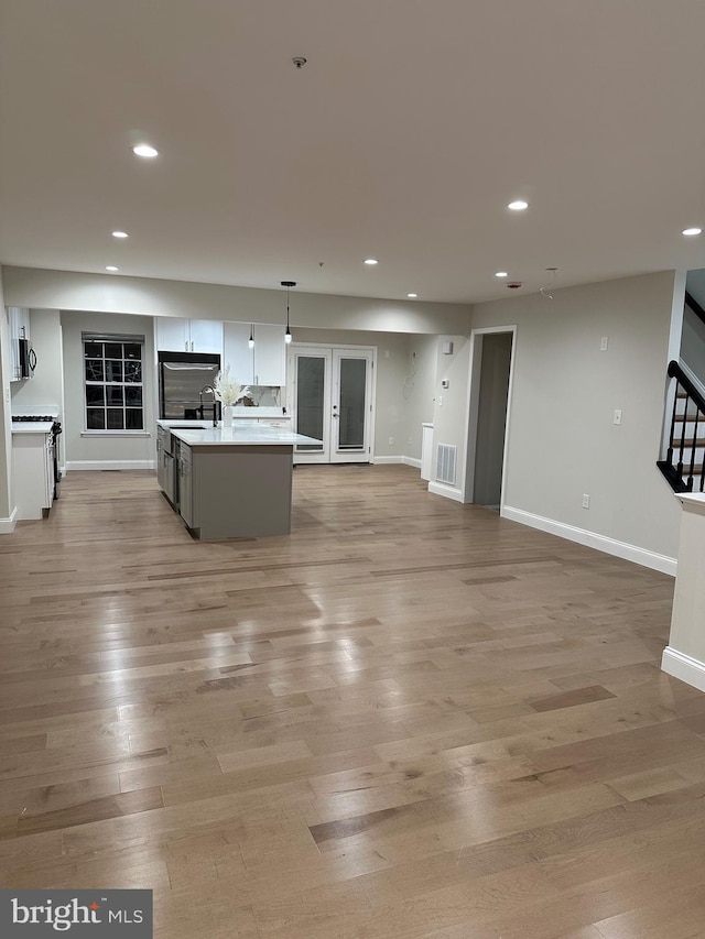 kitchen with sink, a kitchen island with sink, hanging light fixtures, and light wood-type flooring