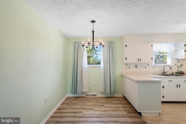 unfurnished dining area with an inviting chandelier, light hardwood / wood-style floors, sink, and a textured ceiling