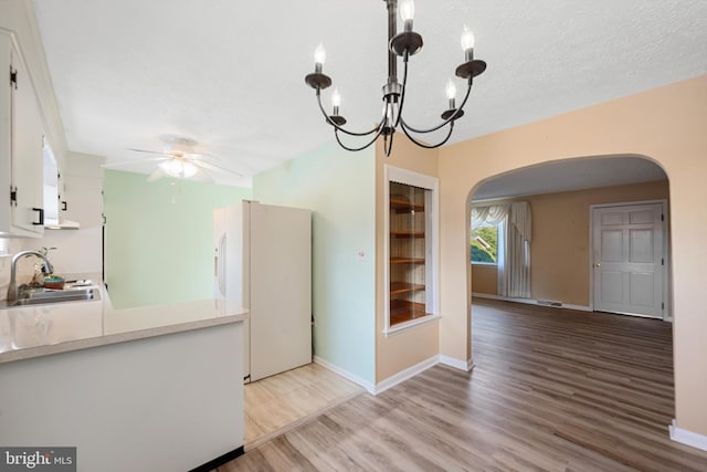 kitchen with ceiling fan with notable chandelier, white cabinetry, sink, white refrigerator with ice dispenser, and light hardwood / wood-style flooring