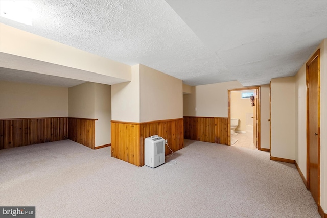 spare room featuring light colored carpet, a textured ceiling, and wooden walls