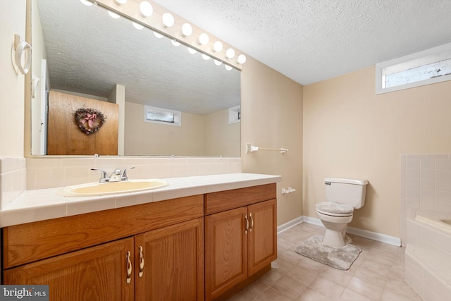 bathroom featuring vanity, tiled tub, a textured ceiling, and toilet