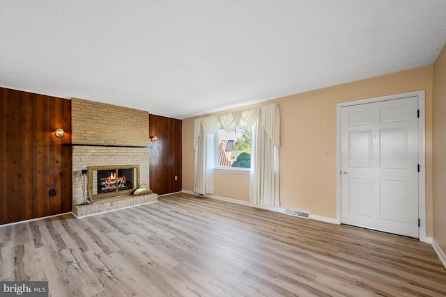 unfurnished living room with a fireplace, wooden walls, and light wood-type flooring