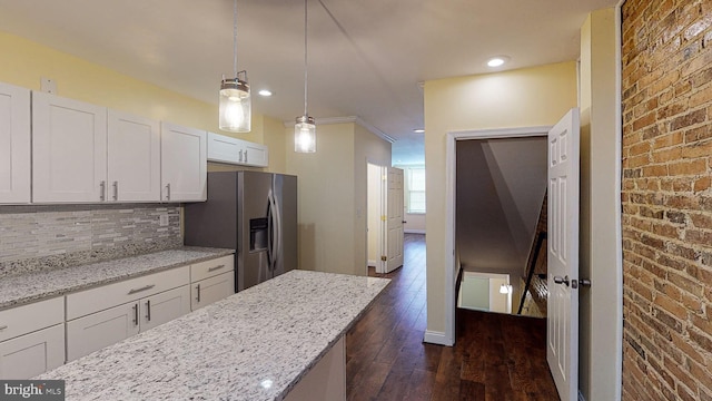 kitchen featuring hanging light fixtures, light stone countertops, brick wall, stainless steel fridge, and white cabinetry