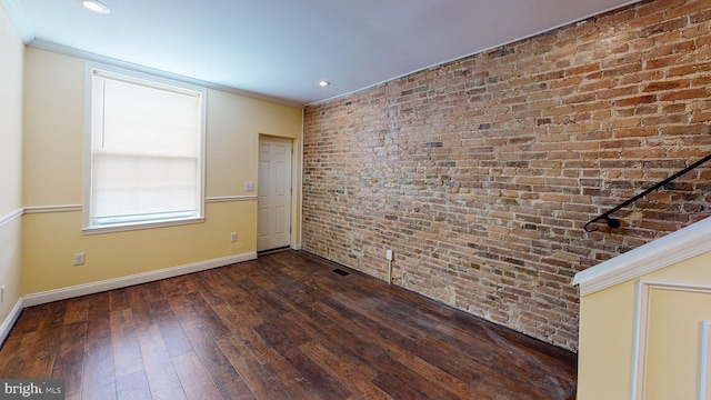 empty room featuring ornamental molding, dark hardwood / wood-style floors, and brick wall