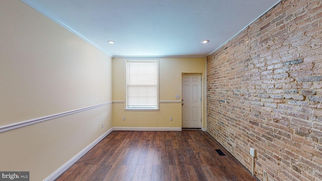 spare room with dark hardwood / wood-style flooring, crown molding, and brick wall