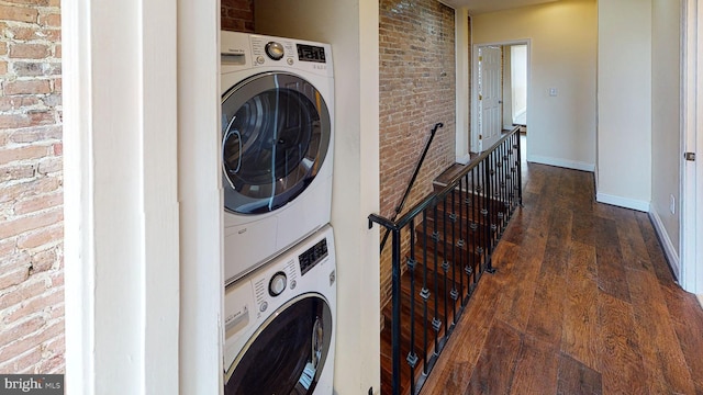 washroom featuring dark hardwood / wood-style flooring, stacked washer / dryer, and brick wall