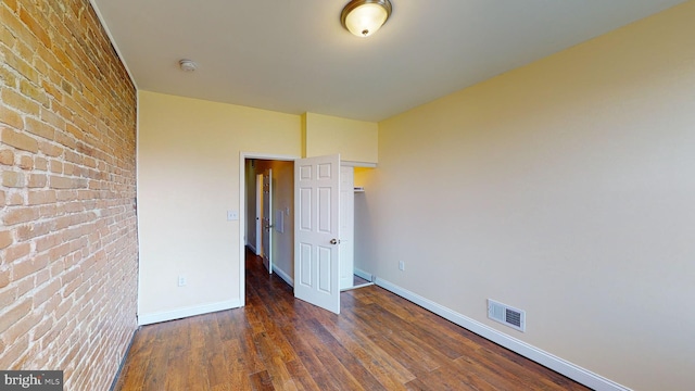 unfurnished bedroom featuring brick wall and dark hardwood / wood-style floors