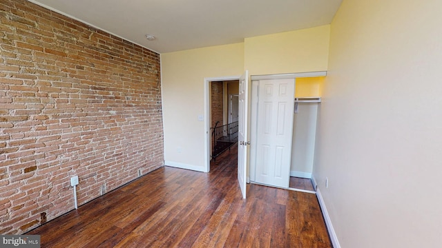 unfurnished bedroom featuring brick wall, dark wood-type flooring, and a closet