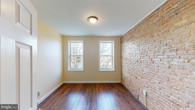 spare room featuring brick wall and dark wood-type flooring