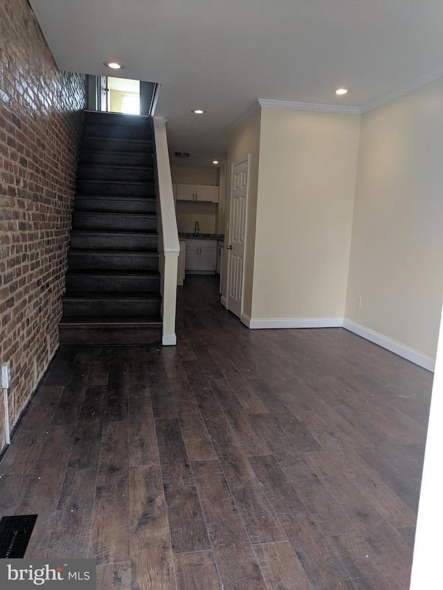 basement featuring brick wall, ornamental molding, and dark hardwood / wood-style flooring