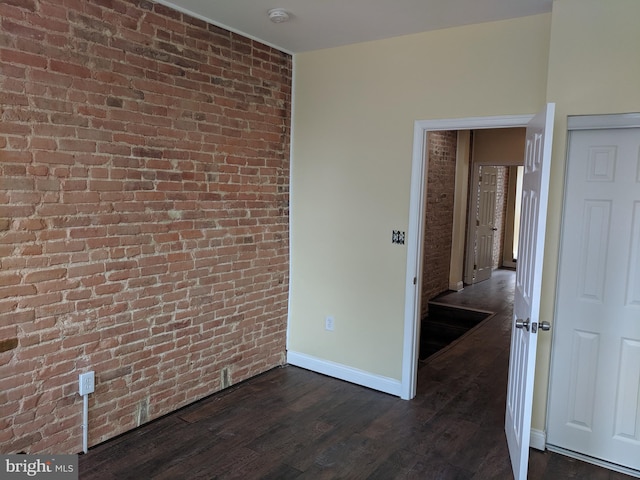 unfurnished room featuring brick wall and dark wood-type flooring