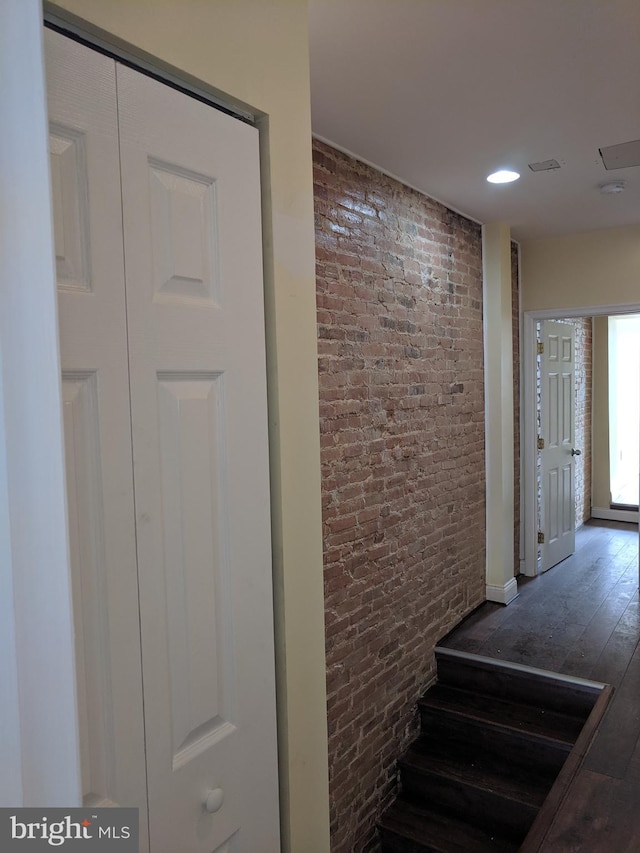 stairway with hardwood / wood-style floors and brick wall