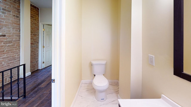 bathroom featuring brick wall and toilet