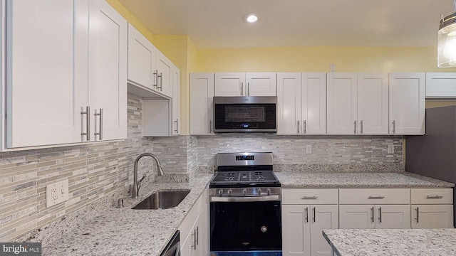 kitchen featuring appliances with stainless steel finishes, light stone countertops, sink, white cabinetry, and backsplash