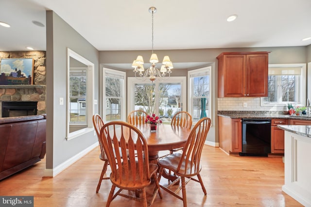 dining room featuring a stone fireplace, light wood-type flooring, an inviting chandelier, and baseboards