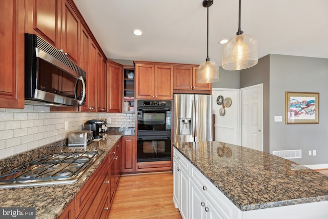 kitchen with stainless steel appliances, visible vents, light wood-style floors, decorative backsplash, and decorative light fixtures