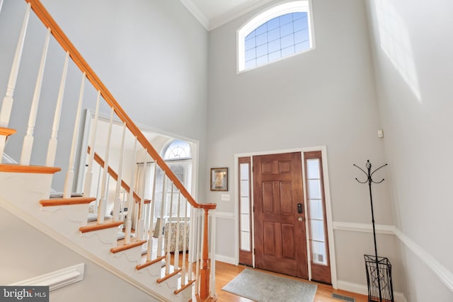 entryway featuring crown molding, a towering ceiling, wood finished floors, baseboards, and stairs