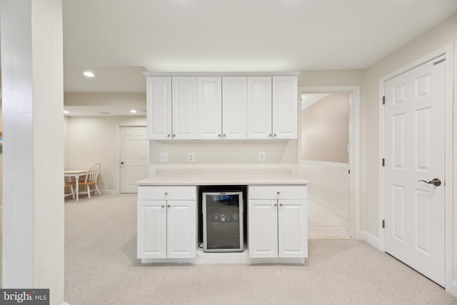 kitchen featuring light carpet, wine cooler, and white cabinetry