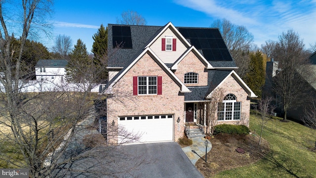 traditional-style home with solar panels, brick siding, an attached garage, and aphalt driveway