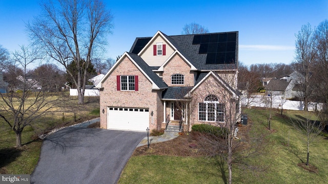 traditional-style home with driveway, a garage, roof with shingles, roof mounted solar panels, and brick siding